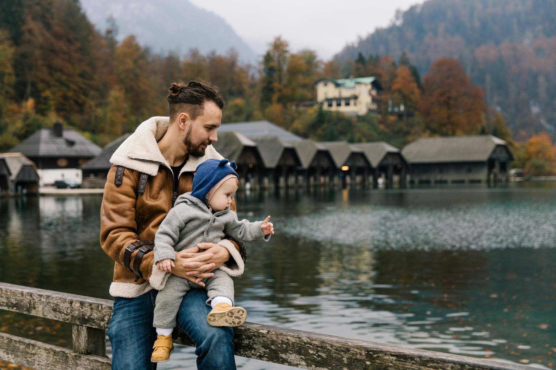 Father holds child by a scenic lake with autumn foliage, enjoying outdoor family time.