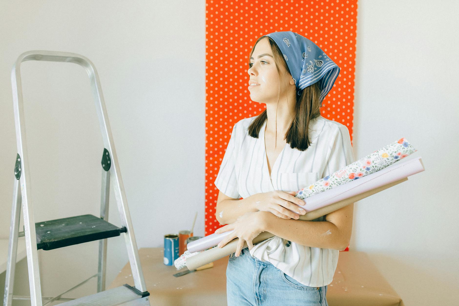 A young woman holding wallpaper is ready for room renovation indoors.