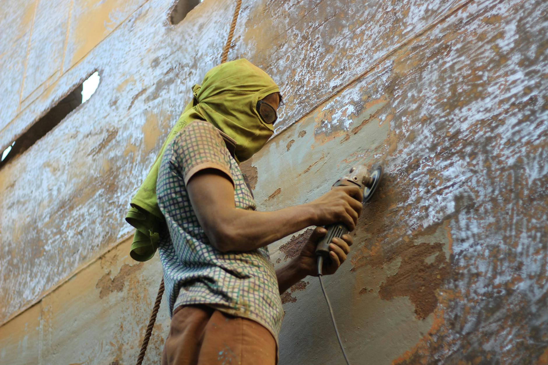 A worker in protective gear grinding a large metal surface at a shipyard.
